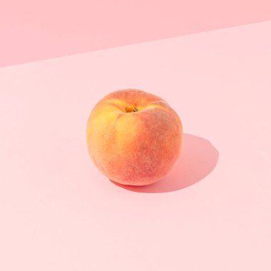 Single ripe peach fruit with sunny day shadow against pastel pink background. Minimal healthy snack food composition.