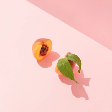 Trendy fresh fruit composition made of cut peach slices with pit and leaves and sunshine shadows. Minimal pastel peach pink background. Creative healthy food concept. Romantic summer party aesthetic.
