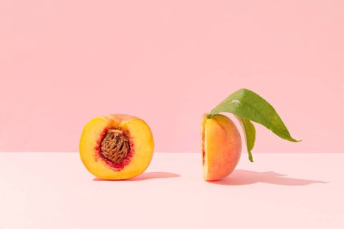 Fresh peach slices with pit and leaves against bright peach pink background. Healthy organic ripe fruits authentic composition.  Artistic food party concept. Trendy healthy eating aesthetic.