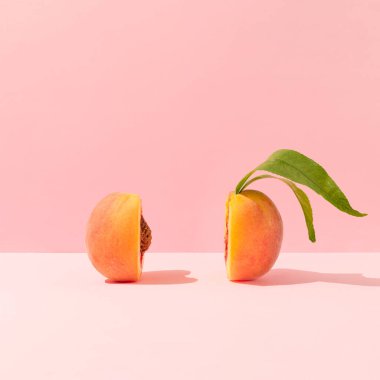 Fresh ripe organic peach with pit and leaves cut in half against bright peach pink background. Minimal fruit concept. Healthy juicy food trendy composition.