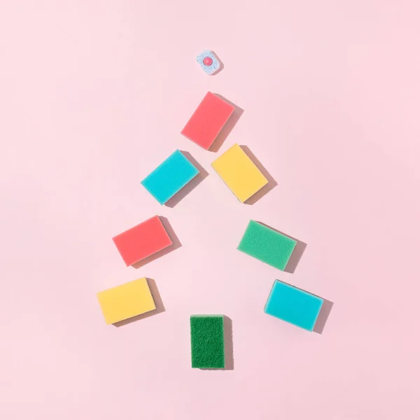 Clolorful cleaning sponges and dishwasher tablet on bright pink background. Minimal Christmas tree shape composition. Trendy Christmas or New Year party cleaning concept.