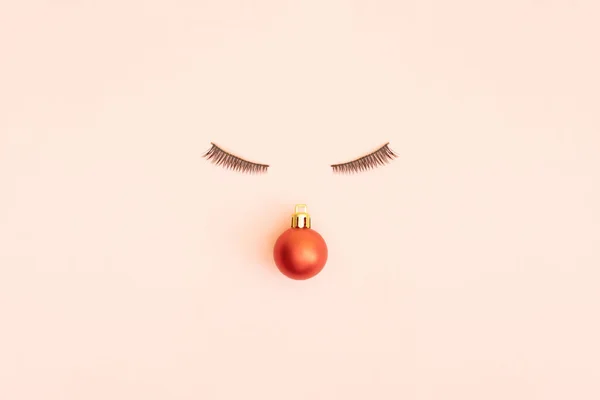 Red bauble with eyelashes on pink pastel background. Minimal design. Copy space.