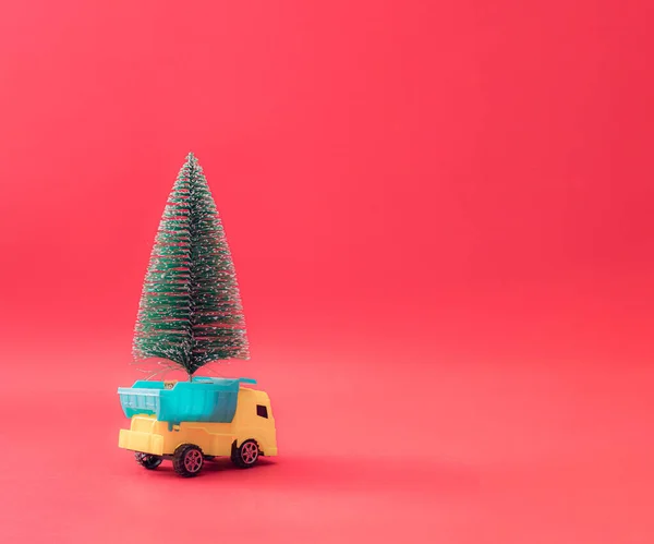 圣诞树在一辆蓝色和黄色的卡车上 红色的粉刷背景 最少的新年场景 — 图库照片