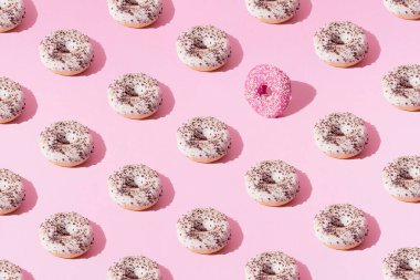 Halkalı çörekler beyaz ve pembe jöleli ve pembe pastel arka planda küçük renkli kırıntılar. Minimum konsept ve tasarım. Şablon. Düz yatıyordu.