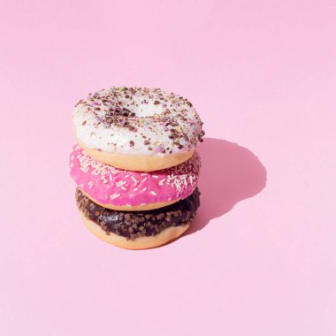 Beyaz, pembe ve çikolata jöleli halka sandviç donutları. Pembe pastel arka planda renkli kırıntılar. Şablon. Boşluğu kopyala.