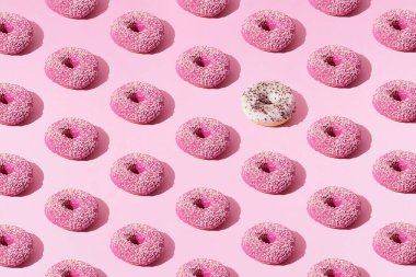 Pembe ve beyaz halka donutlar, jöleli ve pembe pastel arka planda renkli kırıntılar. Desen.