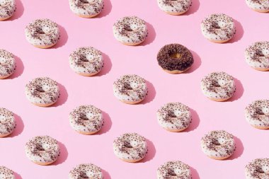 Halkalı çörekler beyaz ve çikolata jöleli ve pembe pastel arka planda küçük renkli kırıntılar. Minimum konsept ve tasarım. Desen.