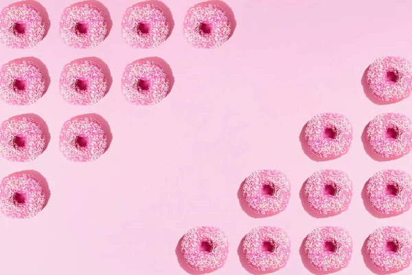 Üçgen şeklinde pembe halka çörekler ve pembe pastel arka planda beyaz kırıntılar. Şablon. Boşluğu kopyala.