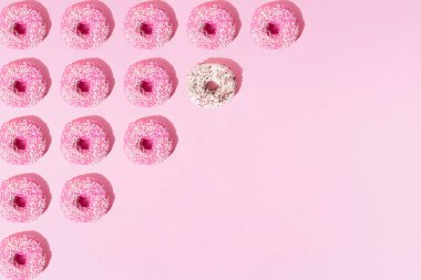 Çikolata kaplı halka çörekler ve pembe pastel arka planda küçük kahverengi kırıntılar. Minimum konsept ve tasarım. Desen.