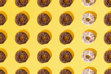 Beyaz ve çikolata jöleli halka çörekler. Sarı pastel arka planda küçük renkli kırıntılar. Şablon. Düz yatıyordu.