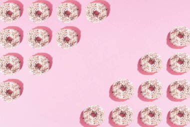 Beyaz jöleli ve pembe pastel arka planda renkli kırıntıları olan üçgen şeklinde düzenlenmiş halka çörekler. Boşluk ve deseni kopyala.