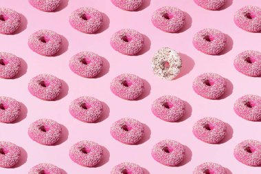 Pembe ve beyaz kaplamalı küçük pembe ve beyaz halka çörekler ve pembe pastel arka planda renkli kırıntılar. Minimum konsept ve tasarım. Desen.