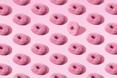 Pembe pastel arka planda jöleli pembe halka çörekler ve beyaz kırıntılar. Desen.