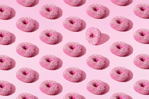 Pembe pastel arka planda jöleli pembe halka çörekler ve beyaz kırıntılar. Desen.
