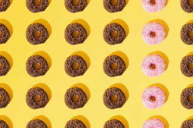 Pembe ve çikolata jöleli halka çörekler. Sarı pastel arka planda küçük beyaz ve kahverengi kırıntılar. Şablon. Düz yatıyordu.