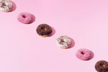 Beyaz, pembe ve çikolata jöleli halka çörekler. Pembe pastel arka planda renkli kırıntılar. Desen.