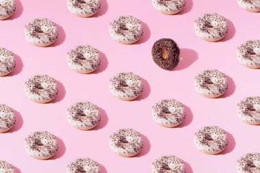 Beyaz ve çikolata kaplı halka çörekler ve pembe pastel arka planda küçük renkli kırıntılar. Minimum konsept ve tasarım. Şablon. Düz yatıyordu.