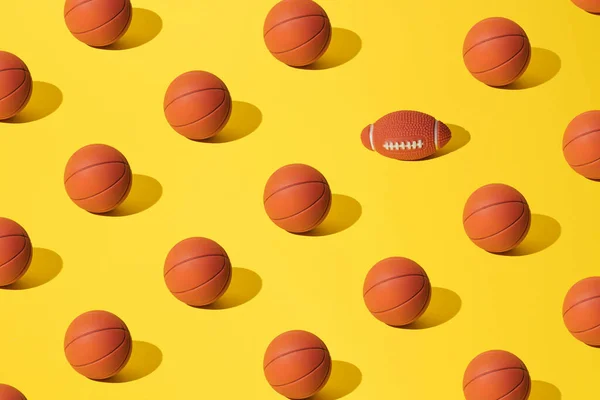 Arranged basketballs on a yellow background with one rugby ball. Pattern.