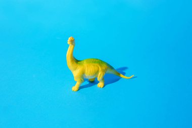 Sarı yeşil plastik oyuncak Brachiosaurus dinozoru mavi arka planda duruyor. Asgari konsept.
