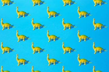 Mavi arka planda sarı yeşil plastik oyuncak Brachiosaurus dinozoru. En küçük desen.