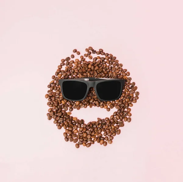 Coffee beans smiley face with glasses. Pink background.