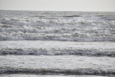 Akşamüstü beyaz arka plan ve gökyüzü ile kumsaldaki deniz dalgalarının resmi