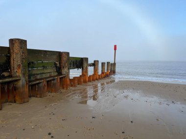 Güzel kumlu sahil manzarası sisli sisli bir sabah Happisburgh Norfolk Doğu Anglia 'da ahşap iskele savunma yapısı ve su yansıması ile kış sabahı sakin bir kış sabahı
