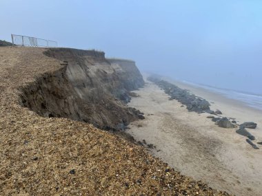 Uçsuz bucaksız kumlu sahil manzarasının kayalar ve sisli manzarası kışın Happisburgh Norfolk 'ta soğuk, nemli ve sisli bir havada sabah mavi gökyüzü olan doğu Anglikan' da.