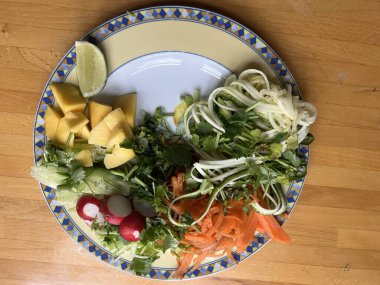 Sağlıklı vejetaryen çiğ sebze yemeğini havuç salatalıklı kişniş turplu, limonlu, soğanlı ve acılı soslu, ahşap yüzey içi düz tabakta.