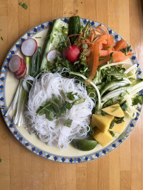 Sağlıklı vejetaryen çiğ sebzeli tofu ve havuç salatalıklı turp turplu soğan ve biber soslu erişteli erişteyle ahın dış yüzeyine düz tabak görünümü yakın.