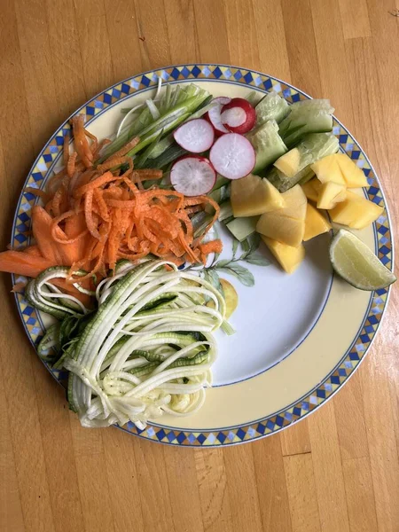 Sağlıklı vejetaryen çiğ sebze yemeğini havuç salatalıklı kişniş turplu, limonlu, soğanlı ve acılı soslu, ahşap yüzey içi düz tabakta.