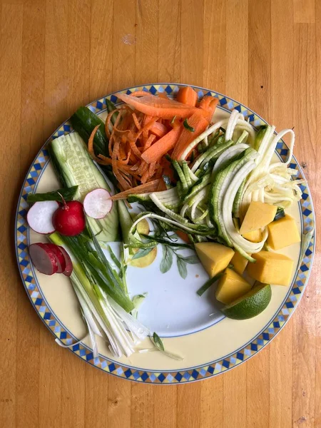 Sağlıklı vejetaryen çiğ sebze yemeğini havuç salatalıklı kişniş turplu, limonlu, soğanlı ve acılı soslu, ahşap yüzey içi düz tabakta.