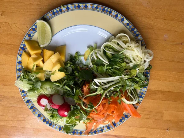 Sağlıklı vejetaryen çiğ sebze yemeğini havuç salatalıklı kişniş turplu, limonlu, soğanlı ve acılı soslu, ahşap yüzey içi düz tabakta.