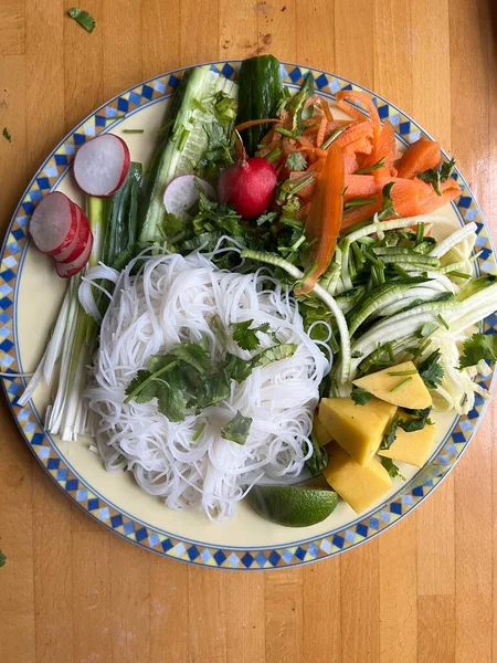 Sağlıklı vejetaryen çiğ sebzeli tofu ve havuç salatalıklı turp turplu soğan ve biber soslu erişteli erişteyle ahın dış yüzeyine düz tabak görünümü yakın.