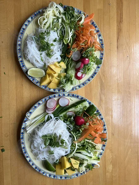 İki tabak sağlıklı vejetaryen çiğ sebze yemeğini havuçlu, kişniş turplu, limonlu, soğanlı ve acılı soslu, ahşap yüzeye düz bir tabakla yakın tut.