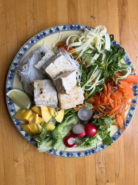 Sağlıklı vejetaryen çiğ sebze yemeğini havuç salatalıklı kişniş turplu, limonlu, soğanlı ve acılı soslu, ahşap yüzey içi düz tabakta.