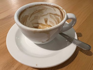 Ekspres kahveyi beyaz porselen bardakta kapayın çay kaşığıyla çay fincanını ve kafein içeceğini bitirin ve kışın tatilde otel restoranındaki ahşap masanın arka planına sürün.