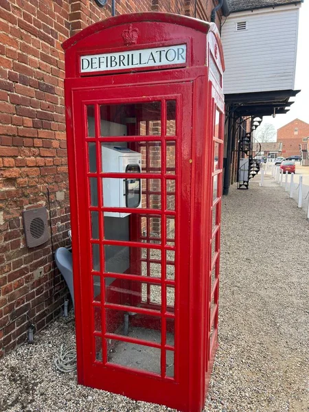 Close up of defibrillator machine public access point for heart attack emergencies stored in iconic traditional red phone box for easy emergency help with telephone sign one side defibrillator other