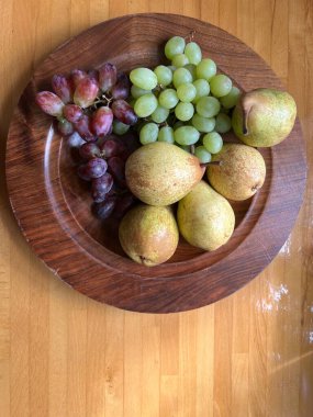 Eldeki meyvelerin yakın konumu armut, yeşil ve kırmızı üzümlü ahşap tabağa dönüştü. Olgun çiğ meyveler vejetaryen salata çöl tabağı için hazır. Gün ışığında düz bir görüş.