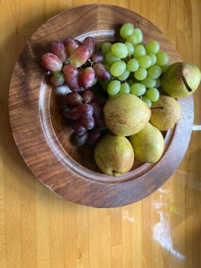Eldeki meyvelerin yakın konumu armut, yeşil ve kırmızı üzümlü ahşap tabağa dönüştü. Olgun çiğ meyveler vejetaryen salata çöl tabağı için hazır. Gün ışığında düz bir görüş.