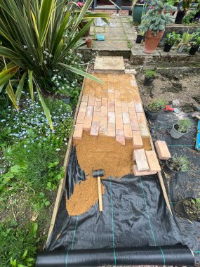 Geri kazanılmış kil, sarı ve kırmızı antika ev taşlarından oluşan tuğla yolu kapatın. Siyah çarşaflı düz bir bahçe yolu inşa edin. Çimlerin altında bitkiler ve çevreleyen çimenler olsun. 