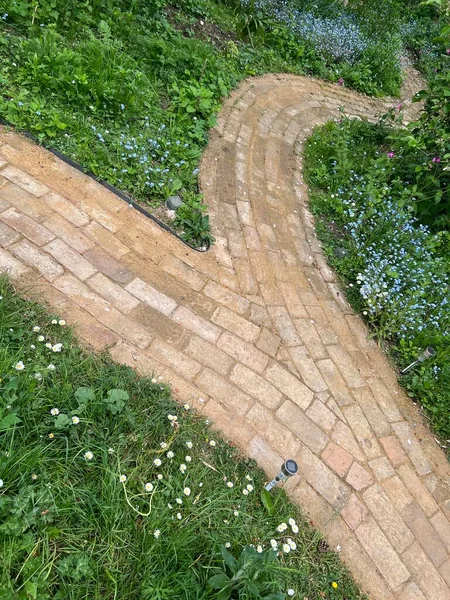 Close up of brick path built with reclaimed clay antique vintage house cream bricks to build windy pathway through wild flower meadow in orchard allotment organic garden with plants and grass borders