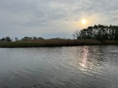 Şafak vakti koro teknesinin güzel manzarası gün doğumunda Hickling Geniş Doğa Koruma Alanı Norfolk Doğu Anglia 'da güneş doğarken bulutların arasından geçerek sazlıklarla suya yansıyor.