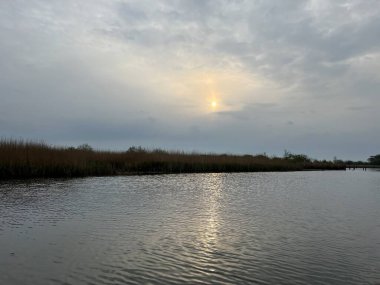 Şafak vakti koro teknesinin güzel manzarası gün doğumunda Hickling Geniş Doğa Koruma Alanı Norfolk Doğu Anglia 'da güneş doğarken bulutların arasından geçerek sazlıklarla suya yansıyor.