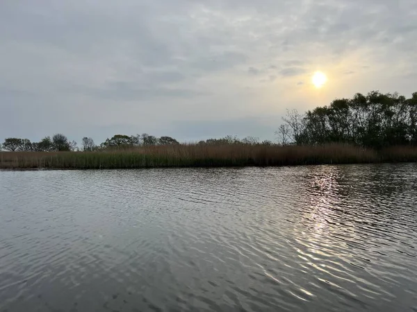 Şafak vakti koro teknesinin güzel manzarası gün doğumunda Hickling Geniş Doğa Koruma Alanı Norfolk Doğu Anglia 'da güneş doğarken bulutların arasından geçerek sazlıklarla suya yansıyor.