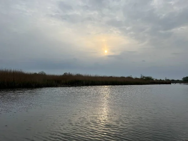 Şafak vakti koro teknesinin güzel manzarası gün doğumunda Hickling Geniş Doğa Koruma Alanı Norfolk Doğu Anglia 'da güneş doğarken bulutların arasından geçerek sazlıklarla suya yansıyor.