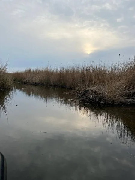 Şafak vakti koro teknesinin güzel manzarası gün doğumunda Hickling Geniş Doğa Koruma Alanı Norfolk Doğu Anglia 'da güneş doğarken bulutların arasından geçerek sazlıklarla suya yansıyor.