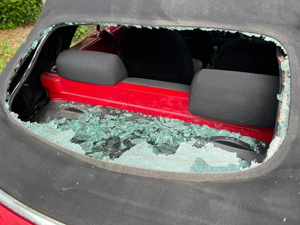 Close up of car accident smashed rear heated glass window on mohair black soft top convertible VW roof with view through hole to automobile interior and back seats with accident shattered pieces