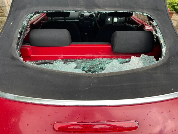 Close up of car accident smashed rear heated glass window on mohair black soft top convertible VW roof with view through hole to automobile interior and back seats with accident shattered pieces