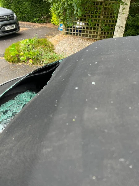 Close up of car accident smashed rear heated glass window on mohair black soft top convertible VW roof with view through hole to automobile interior and back seats with accident shattered pieces